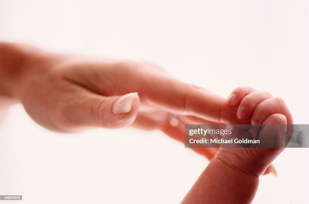 Baby (0-3 months) holding mother's finger with hand, close-up