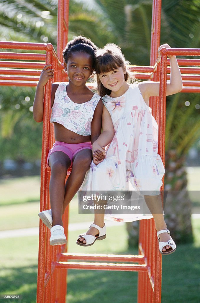Two girls (6-8) playing on climbing frame in park