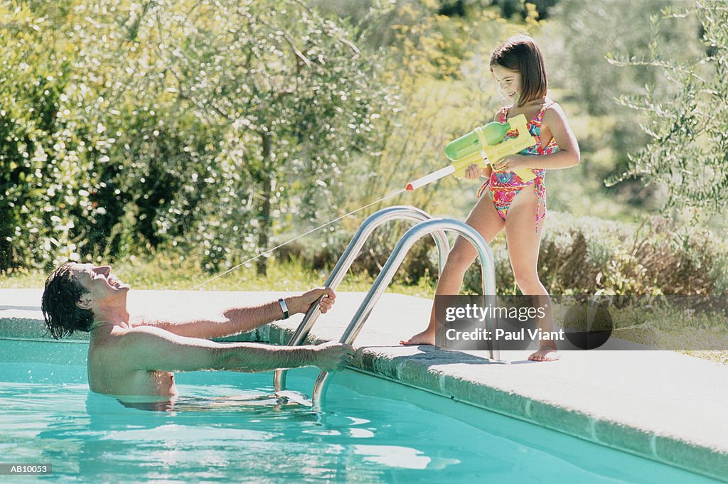 Father in pool while daughter (8-10) using water pistol