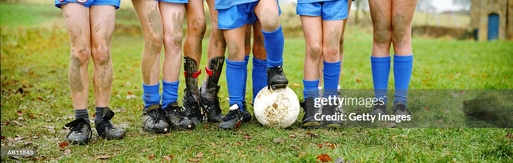 Boys standing in row with soccer ball, muddy legs