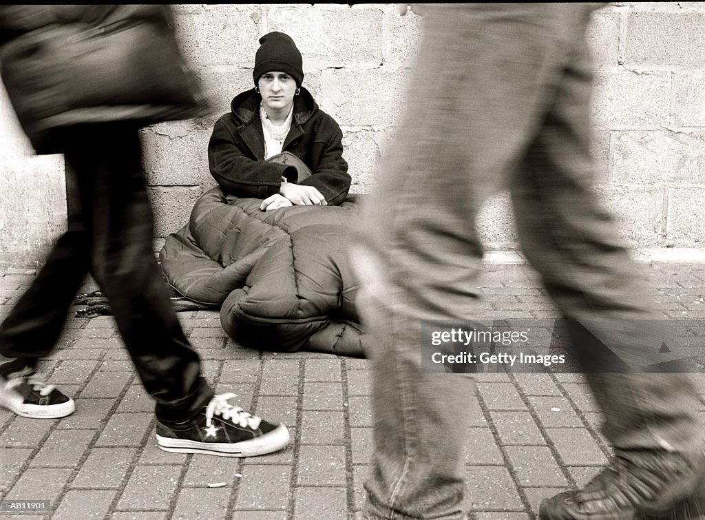 People walking by homless man, sitting on street, (B&W)