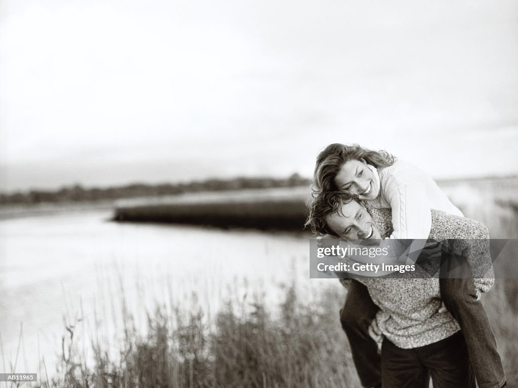 Couple by lake, man giving woman piggy back ride, (B&W)