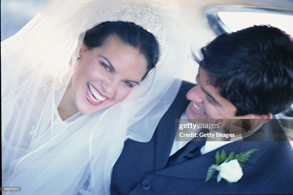 Bride and groom laughing in back of car