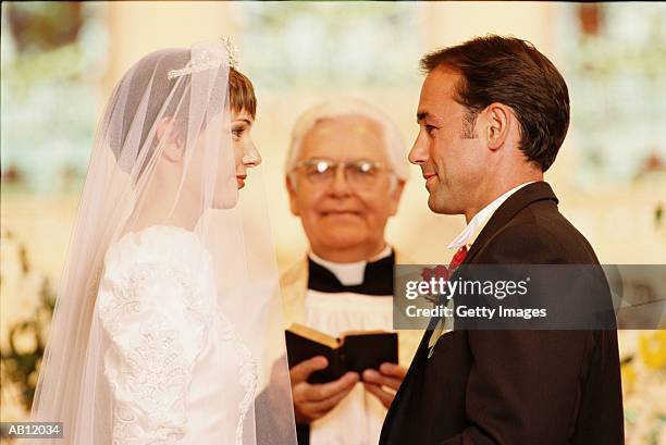 bride and groom with officiate during ceremony in curch - promesas de matrimonio fotografías e imágenes de stock