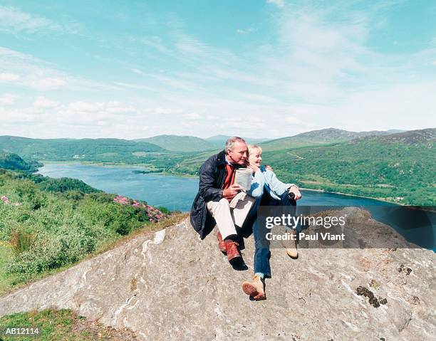 mature couple sitting on rock at top of hill, smiling - rock hill stock pictures, royalty-free photos & images