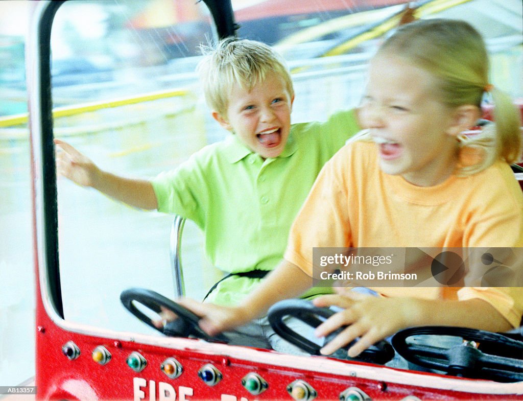 Brother and sister (5-9) driving toy fire truck (blurred motion)