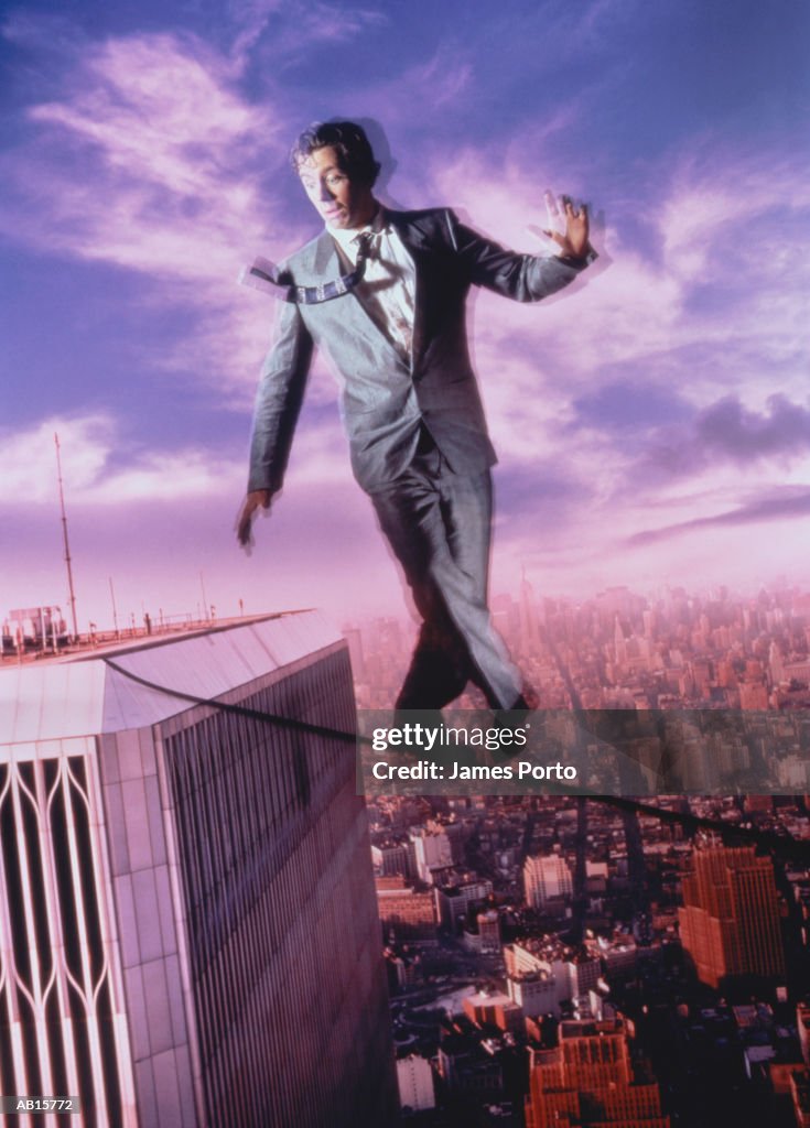 MALE EXECUTIVE ON TIGHTROPE ABOVE CITY.