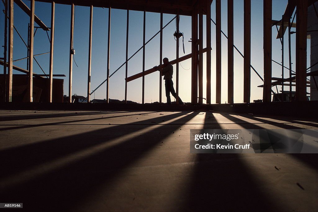 Carpenter carrying lumber at construction site, silhouette