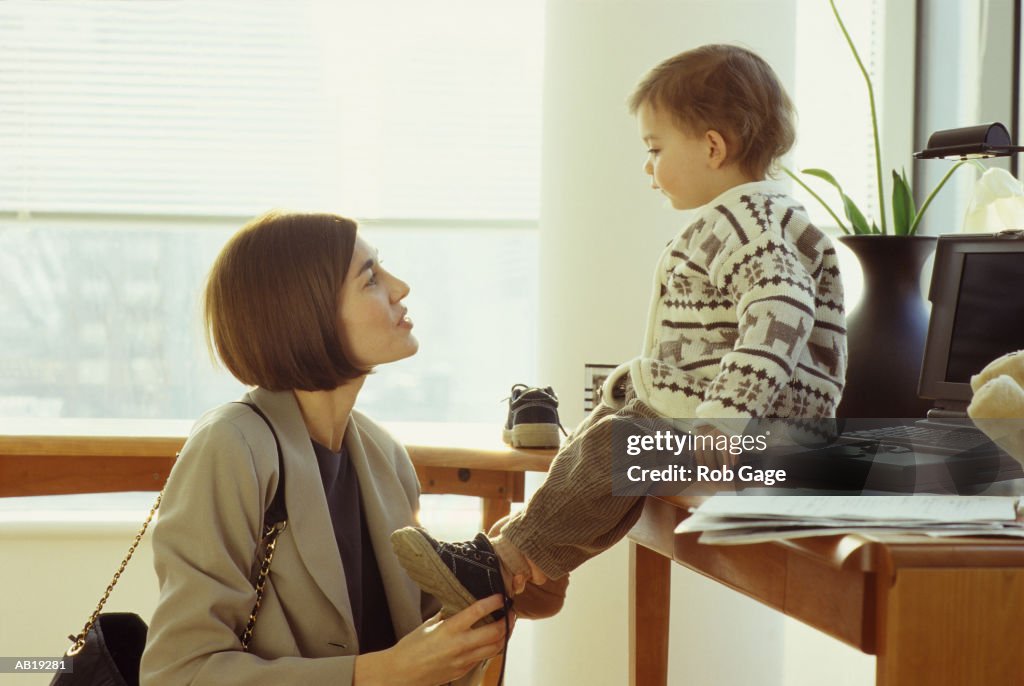 Mother putting toddler boy's (21-24 months) shoes on, in office