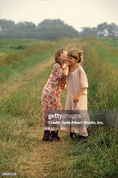 two girls (6-8) whispering to each other in field - albert foto e immagini stock