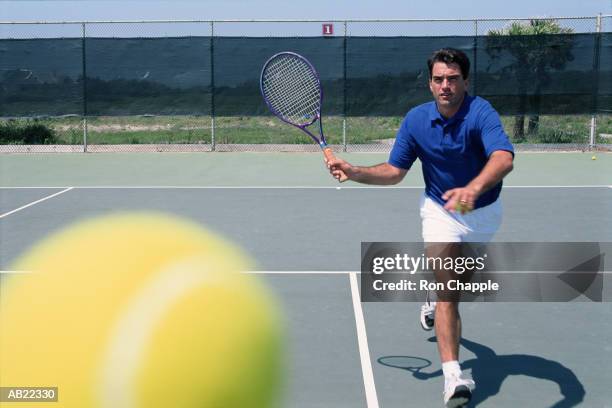 man playing tennis, ball in foreground - amateur tennis man stock pictures, royalty-free photos & images