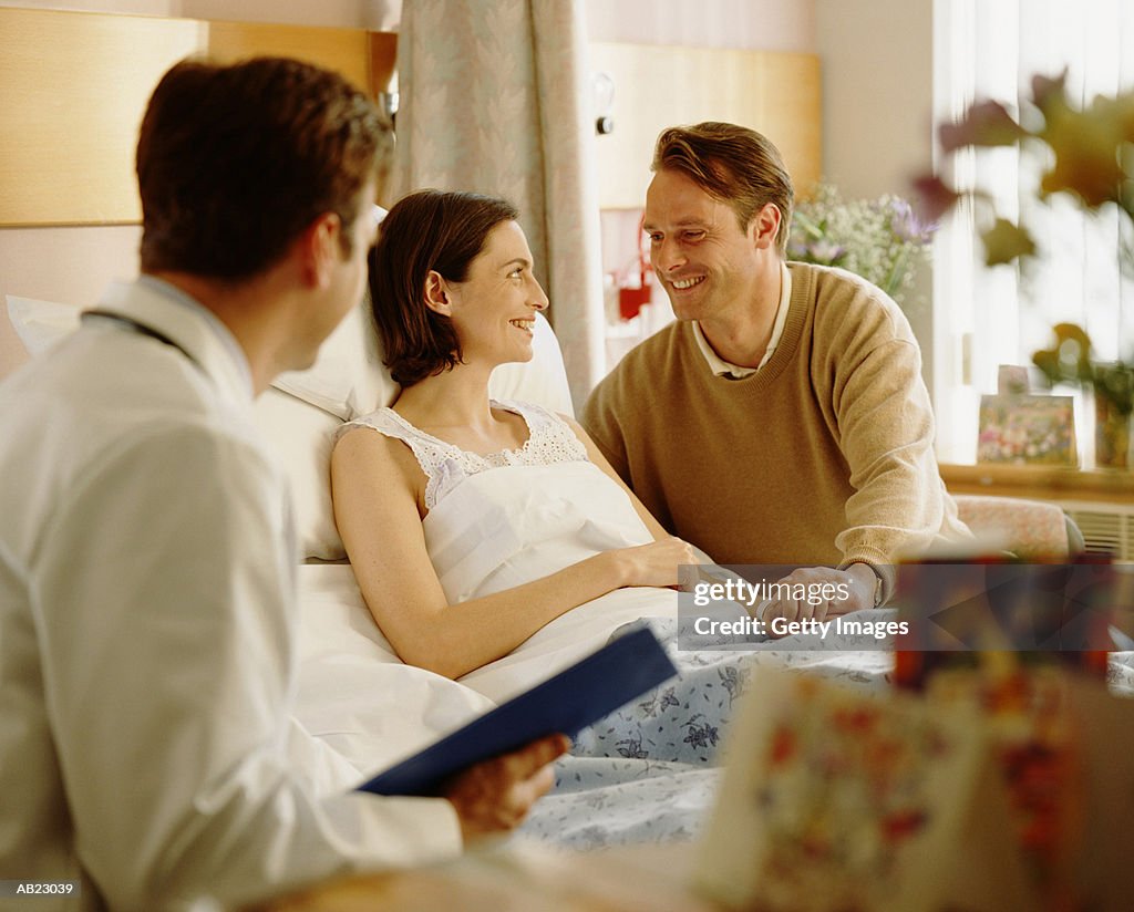 Woman in hospital bed talking with husband, doctor by there side