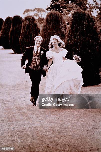 bride and groom running hand in hand in garden, (b&w) - two toned dress stockfoto's en -beelden