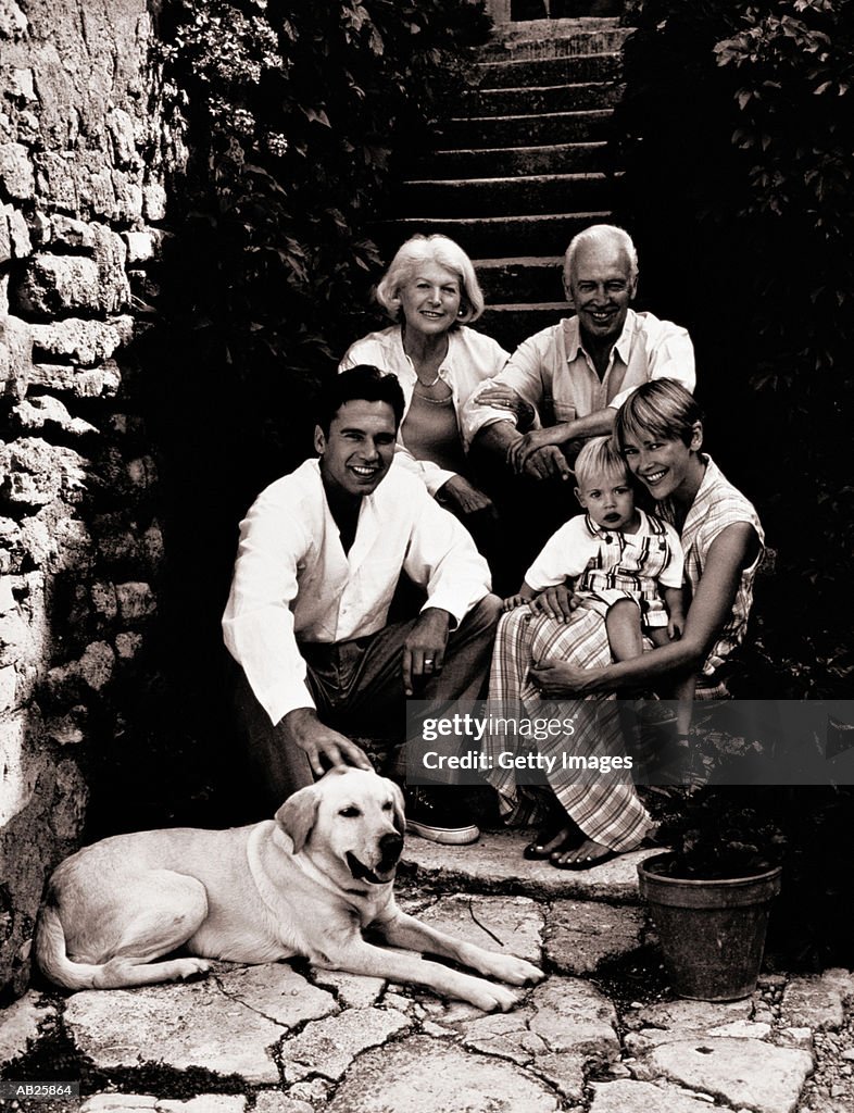 Three generational family sitting on steps with dog, (B&W)