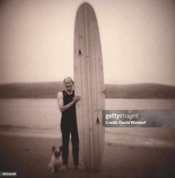 mature man standing with surfboard and dog on beach (soft focus, b&w) - waldorf stock-fotos und bilder