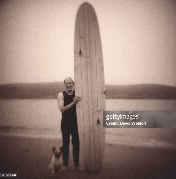 mature man standing with surfboard and dog on beach (soft focus, b&w) - waldorf stock pictures, royalty-free photos & images