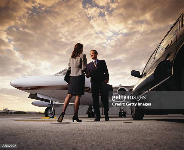 businessman shaking businesswoman's hand, privat jet in background - audi man stockfoto's en -beelden