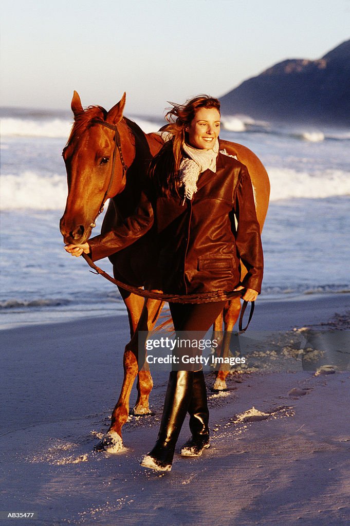 Woman leading horse along beach