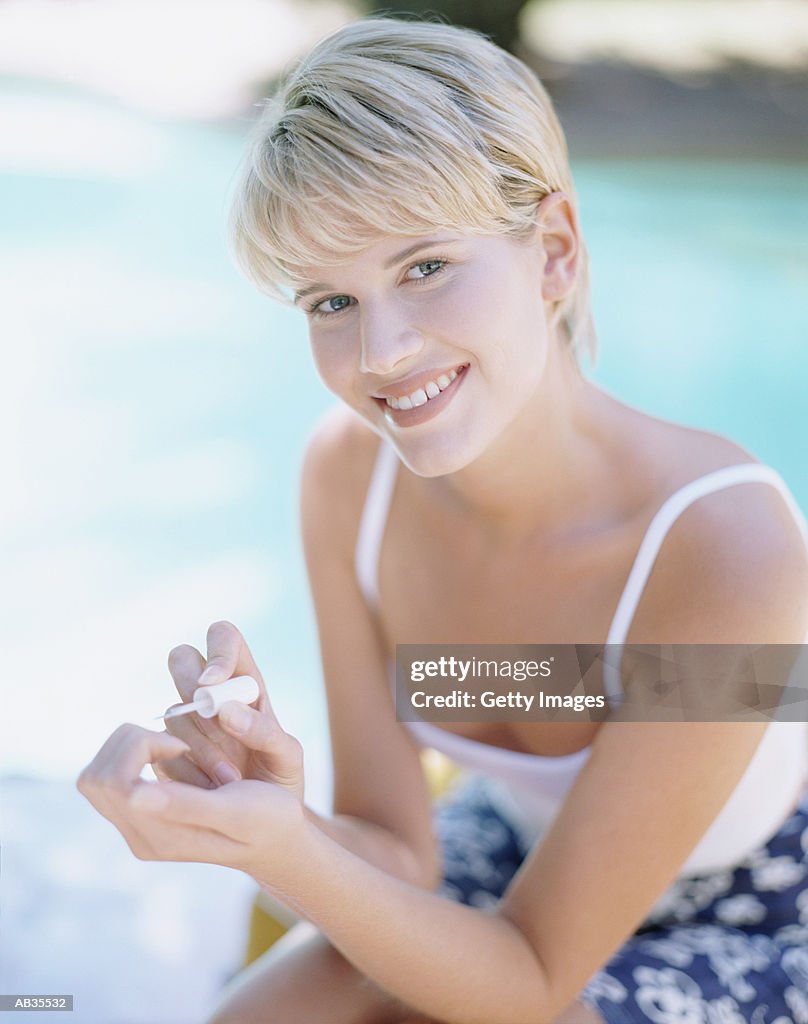 Woman sitting by swimming pool, painting nails, portrait