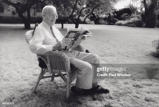 elderly man reading newspaper in wicker chair in yard (b&w) - yard stockfoto's en -beelden
