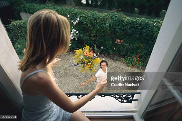 man tossing bouquet of flowers to woman in open window - cantare una serenata foto e immagini stock