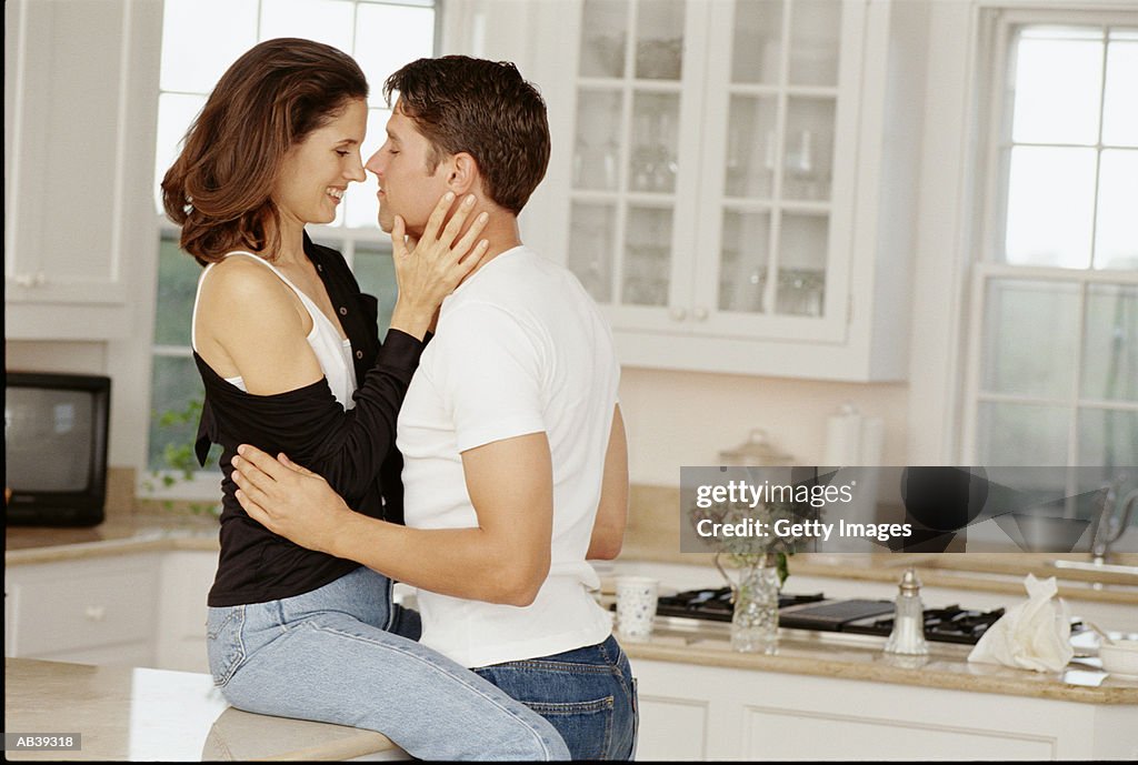 Couple about to kiss embracing in kitchen, woman on counter top