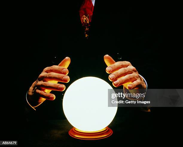 man in suit with hands around glowing crystal ball - forecasting stock-fotos und bilder