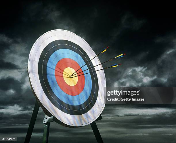 archery target with arrows, dark clouds in background - arco e flecha equipamento desportivo imagens e fotografias de stock