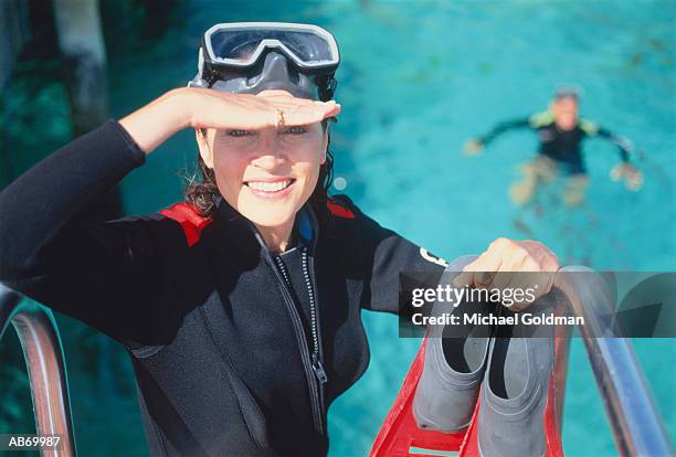 woman in wetsuit about to get into water, man in water below - get stock pictures, royalty-free photos & images