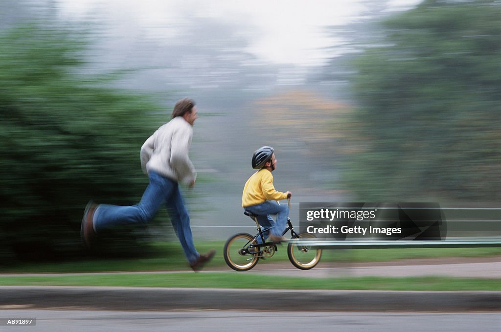 Father running by son (7-9) riding bicycle