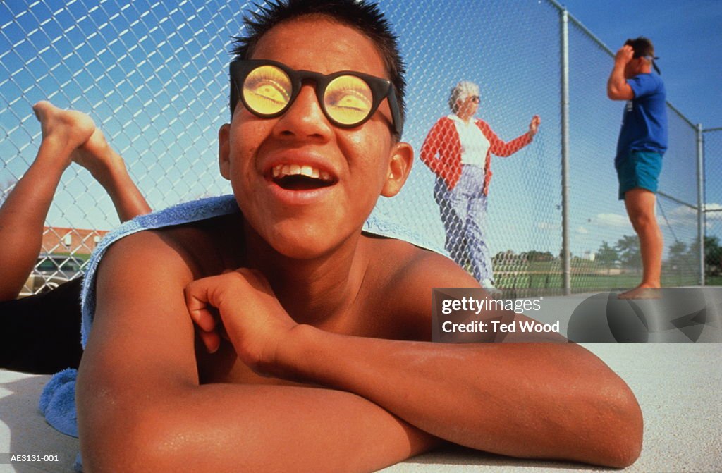 Teenager (14-16) wearing hologram sunglasses, sunbathing