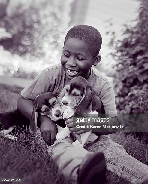 Boy (6-8) sitting on grass playing with puppies, close-up (B&W)