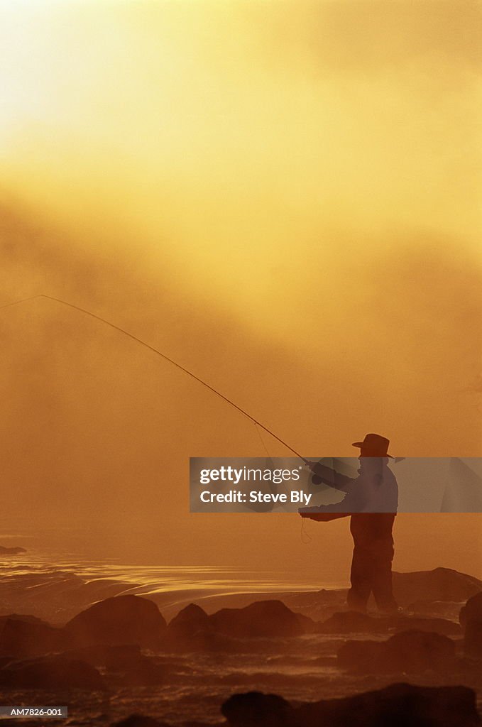 Man fly-fishing, silhouetted in dawn mist, Idaho, USA