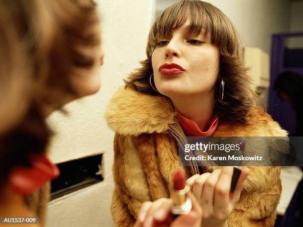 young woman looking at reflection in mirror, holding lipstick - manteau de fourrure photos et images de collection