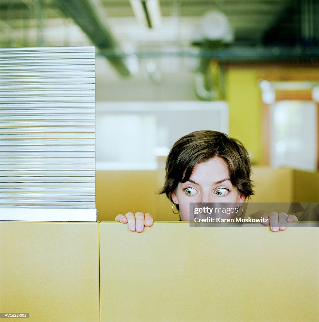 Businesswoman peering over cubicle wall