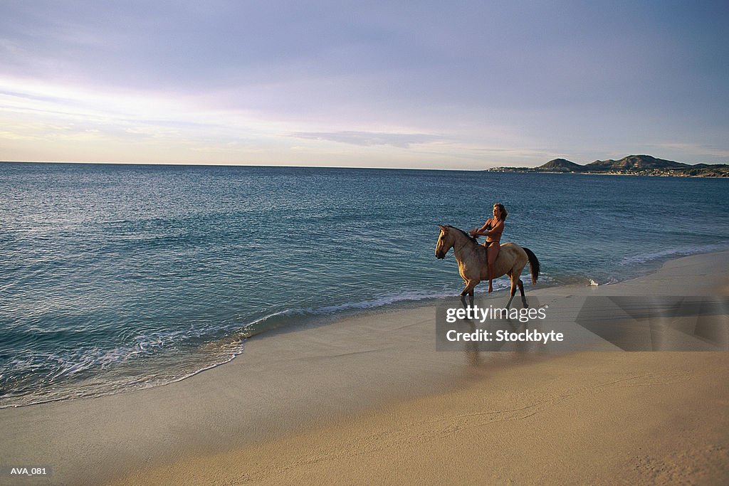Distant shot of woman riding horse on beach