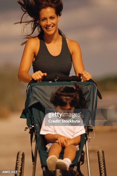 woman running, pushing child in three-wheeled carriage - three wheeled pushchair stock pictures, royalty-free photos & images