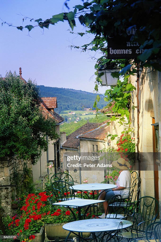 Woman sitting at outdoor cafe overlooking village, elevated view