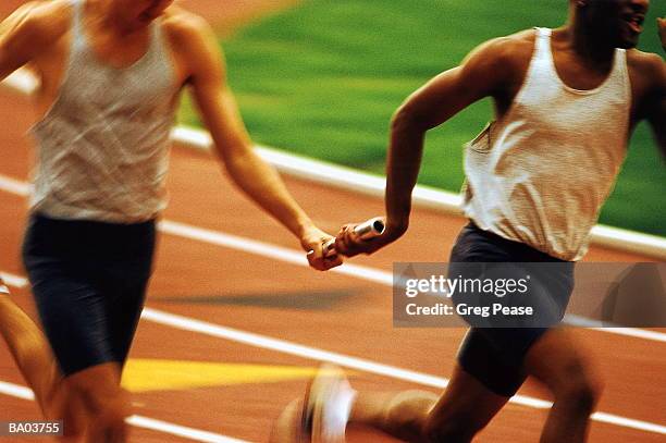 relay racers passing baton, mid section (blurred motion) - stafett bildbanksfoton och bilder
