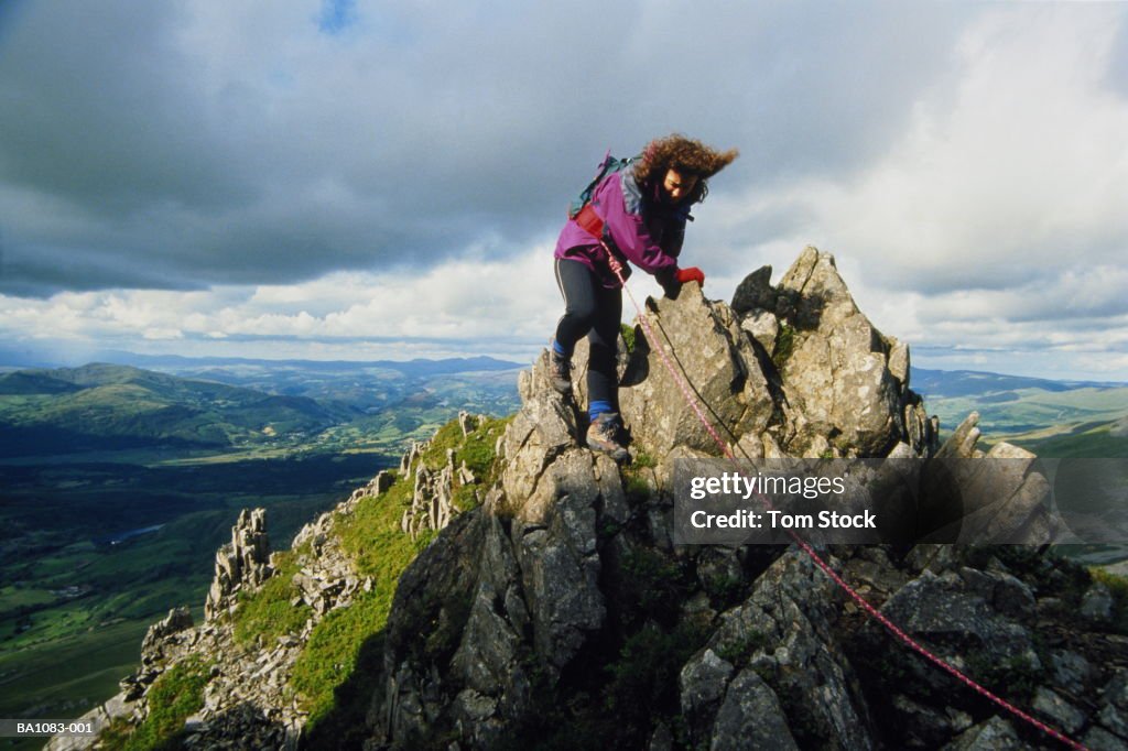 Hiker scaling jagged peak, high over surrounding landscape