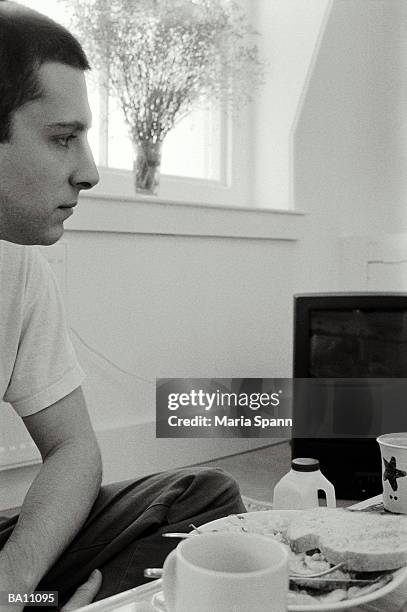young man sitting cross-legged on floor at table, profile (b&w) - maria stockfoto's en -beelden