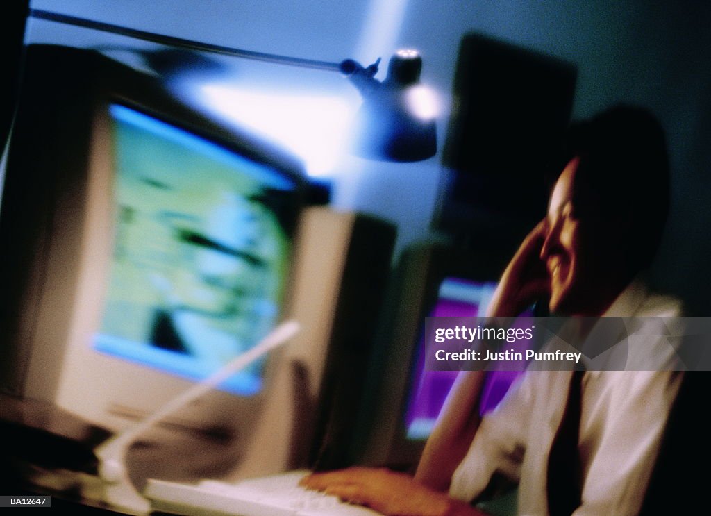 Businessman at desk in front of computer, smiling (defocussed)