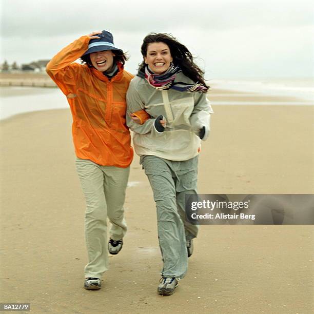 two young women walking on windy beach, laughing - kagoul stock pictures, royalty-free photos & images