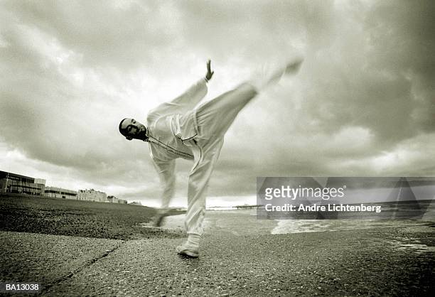 man performing martial arts high kick on beach (b&w) - high kick stock pictures, royalty-free photos & images