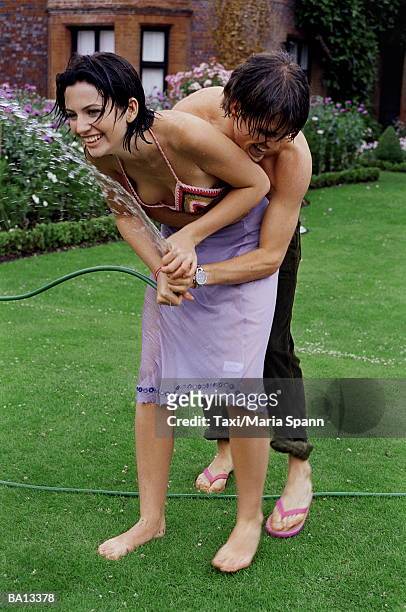 young couple fighting over garden hose - maria stockfoto's en -beelden