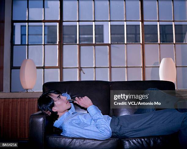 businessman lying on sofa, pen to mouth - antonio stock pictures, royalty-free photos & images