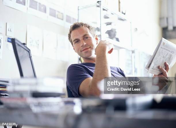 young man sitting at desk holding newspaper, portrait - 20 29 years stock pictures, royalty-free photos & images