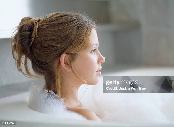 young woman relaxing in bubble bath, profile, close-up - bun hair woman stock pictures, royalty-free photos & images