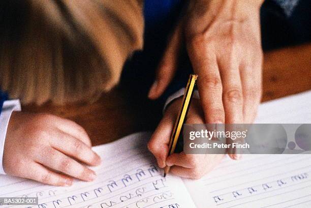 child (5-7) practising writing in book, guided by adult, close-up - links stock-fotos und bilder