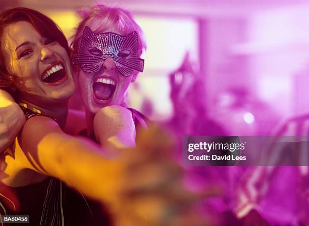 two women embracing at office party, one wearing mask, portrait - máscara-para-fiestas fotografías e imágenes de stock